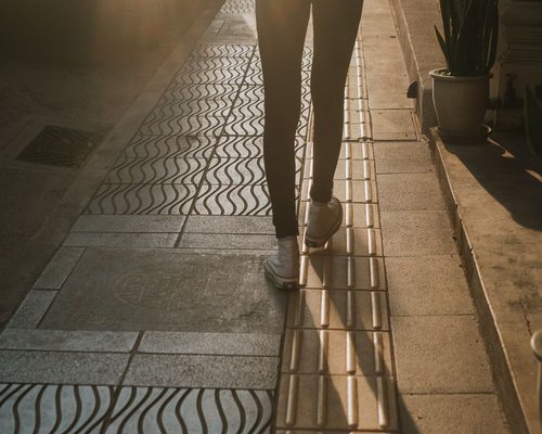 A person wearing comfortable sneakers walking smoothly down a modern urban sidewalk covered with morning light