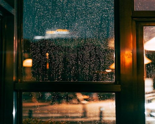 A warm lit room with a wide glass window showing blurred silhouettes of a rainy cityscape, promoting cozy indoor balance